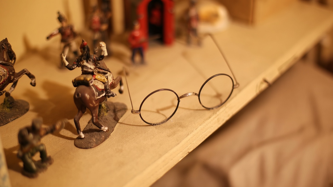 Round wire glasses on a wooden shelf beside small painted toy soldiers